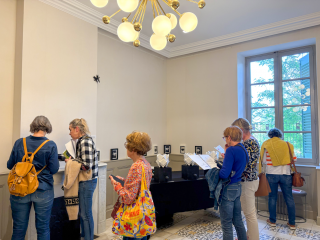 Groupe de visiteurs découvrant une exposition dans une salle intérieure, observant des œuvres et lisant des supports de médiation culturelle