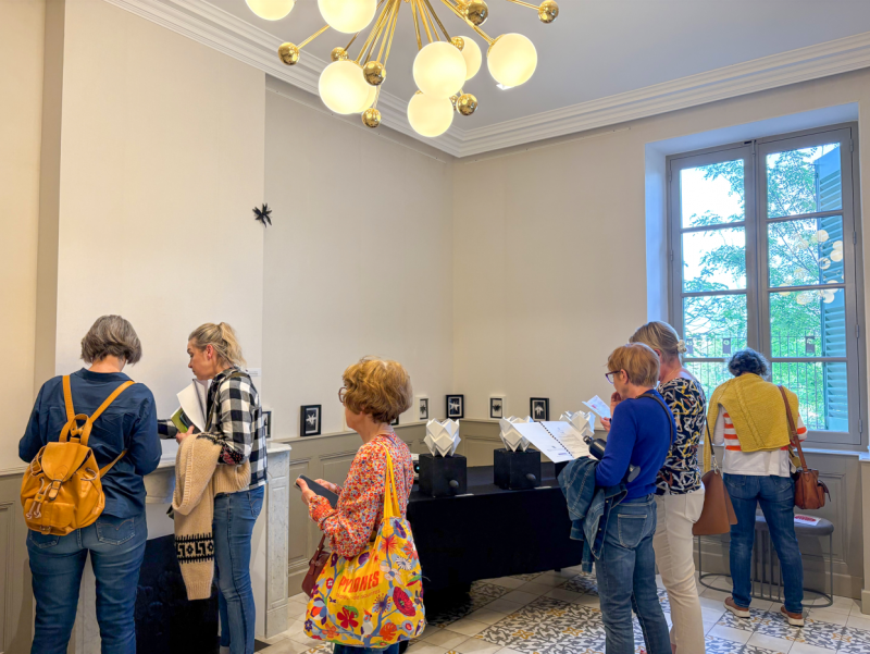 Groupe de visiteurs découvrant une exposition dans une salle intérieure, observant des œuvres et lisant des supports de médiation culturelle